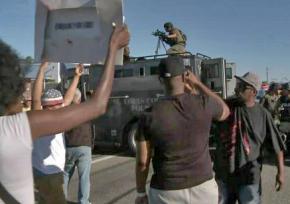 Police equipped with machine guns confront protesters in Ferguson, Mo.train machine guns on a crowd of protesters in broad daylight